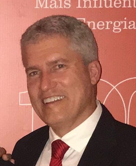 O gerente William Souza, branco, cabelo grisalho, sorri de terno preto, camisa branca e gravata vermelha