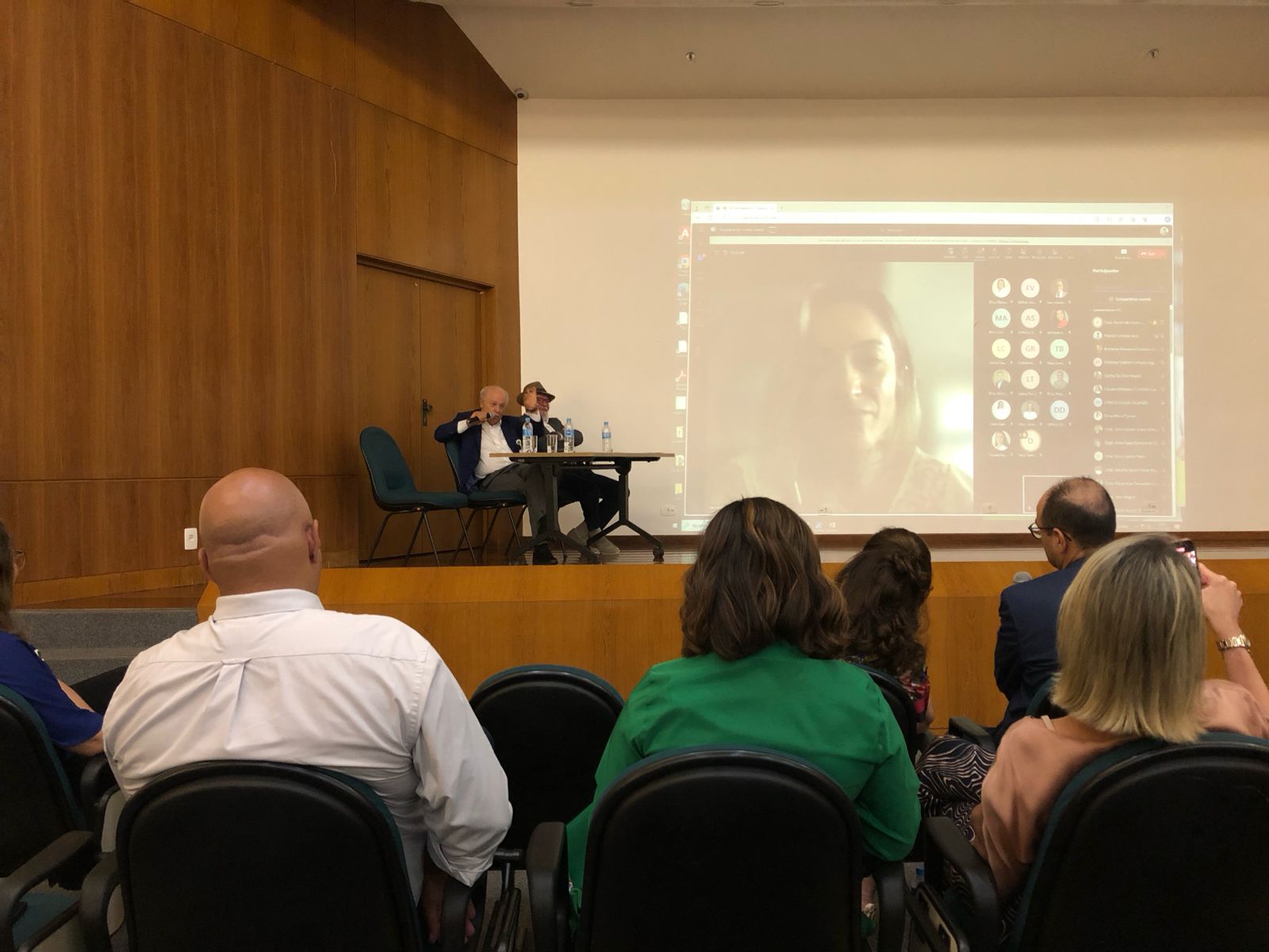 Dois médicos sentados em cadeiras em cima de um palco respondendo à perguntas