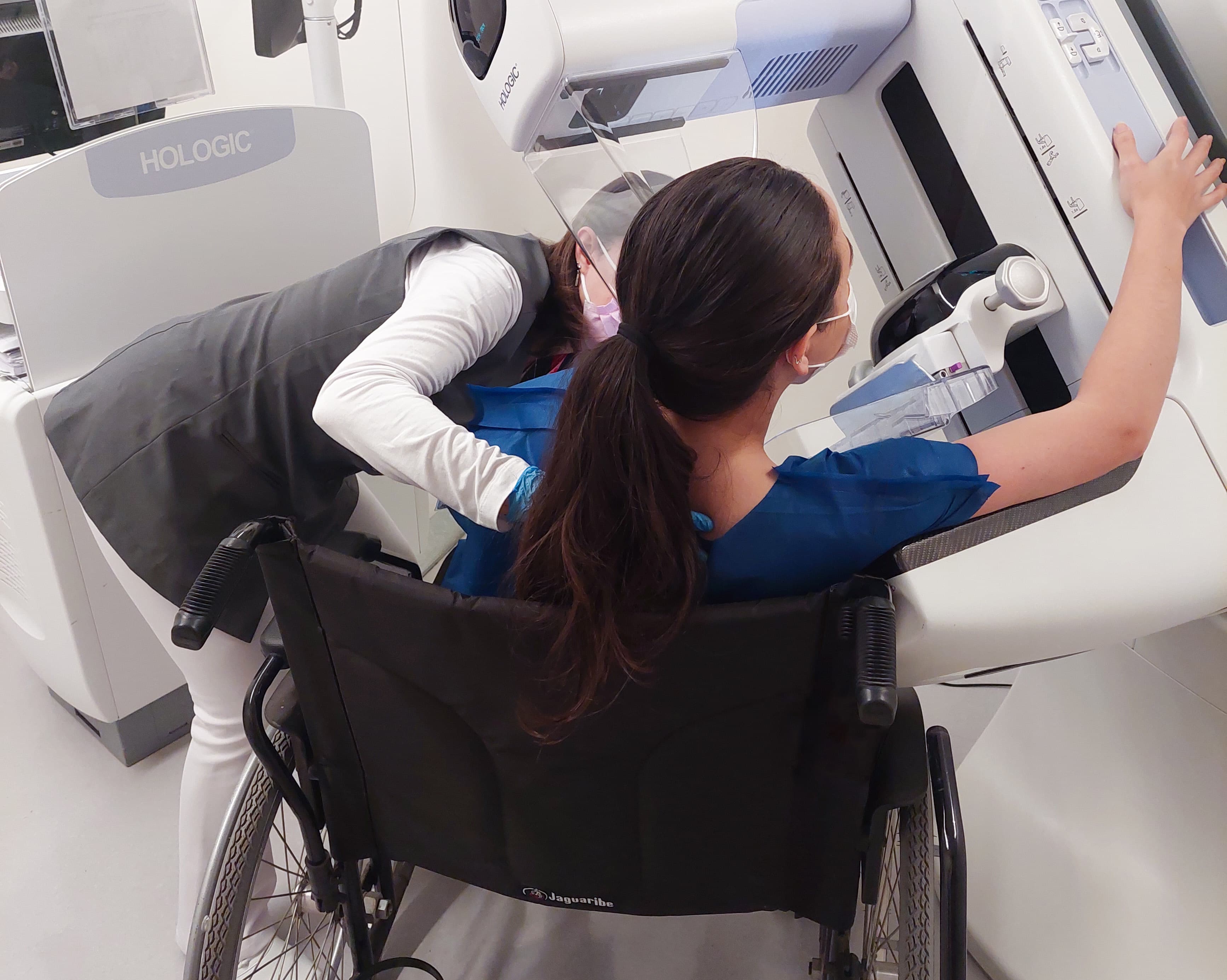 Pessoas com deficiência: moça branca sentada na cadeira de rodas com o mamógrafo abaixado