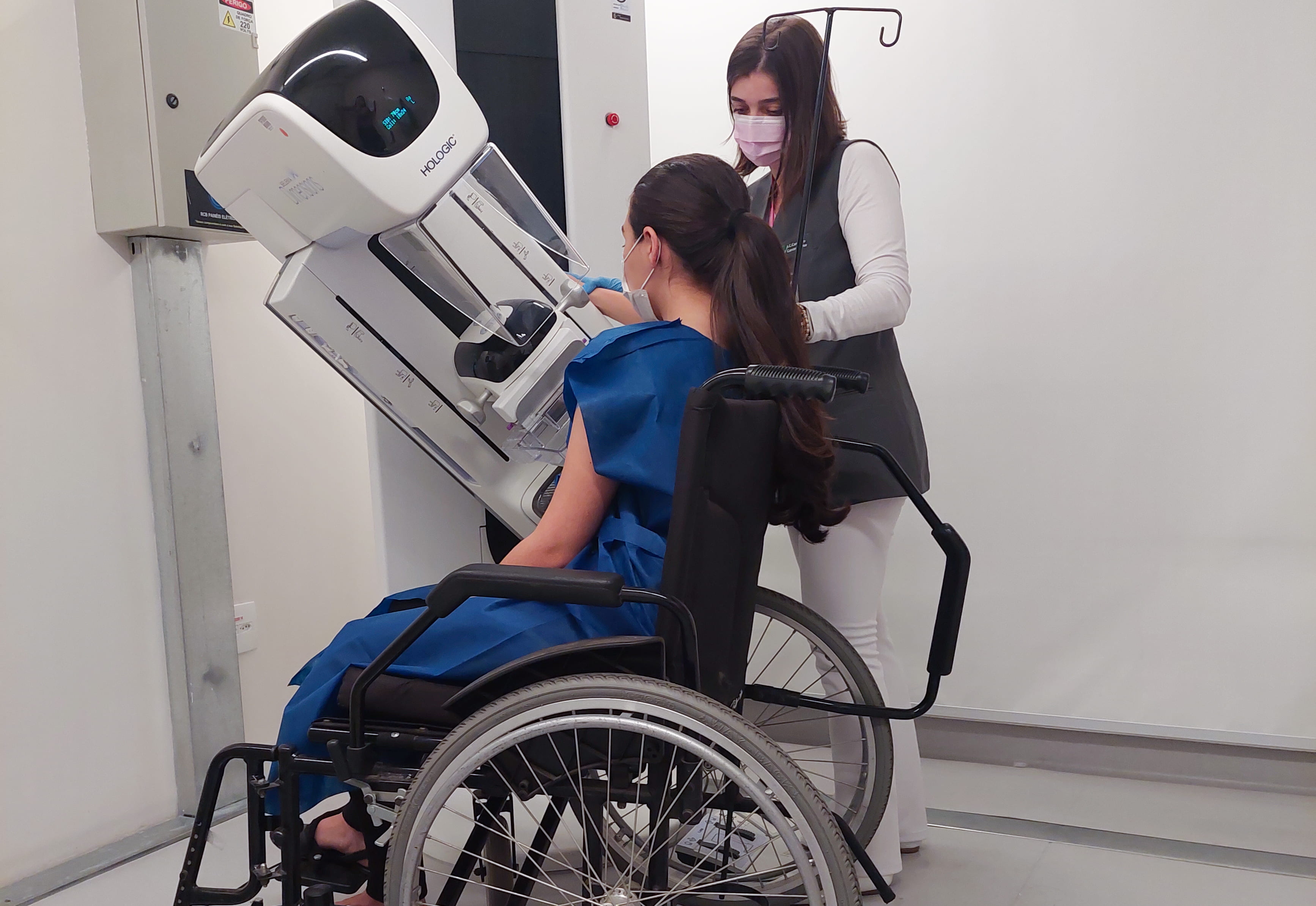 Pessoas com deficiência: moça branca sentada na cadeira de rodas com o mamógrafo abaixado