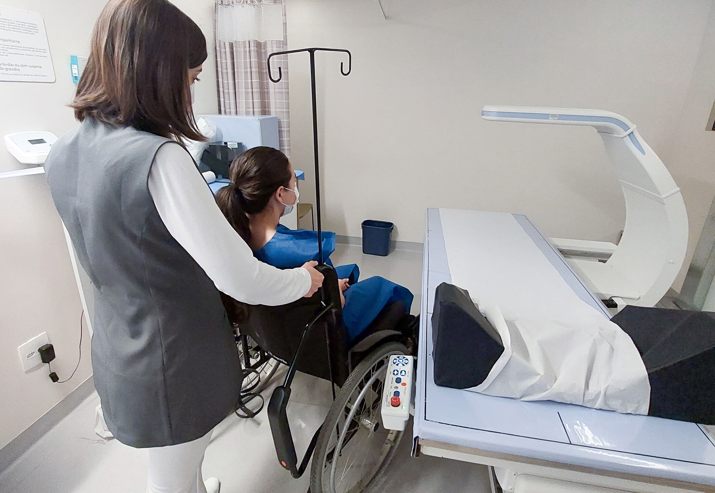 Pessoas com deficiência: moça branca sentada na cadeira de rodas ao lado da mesa de raio-x