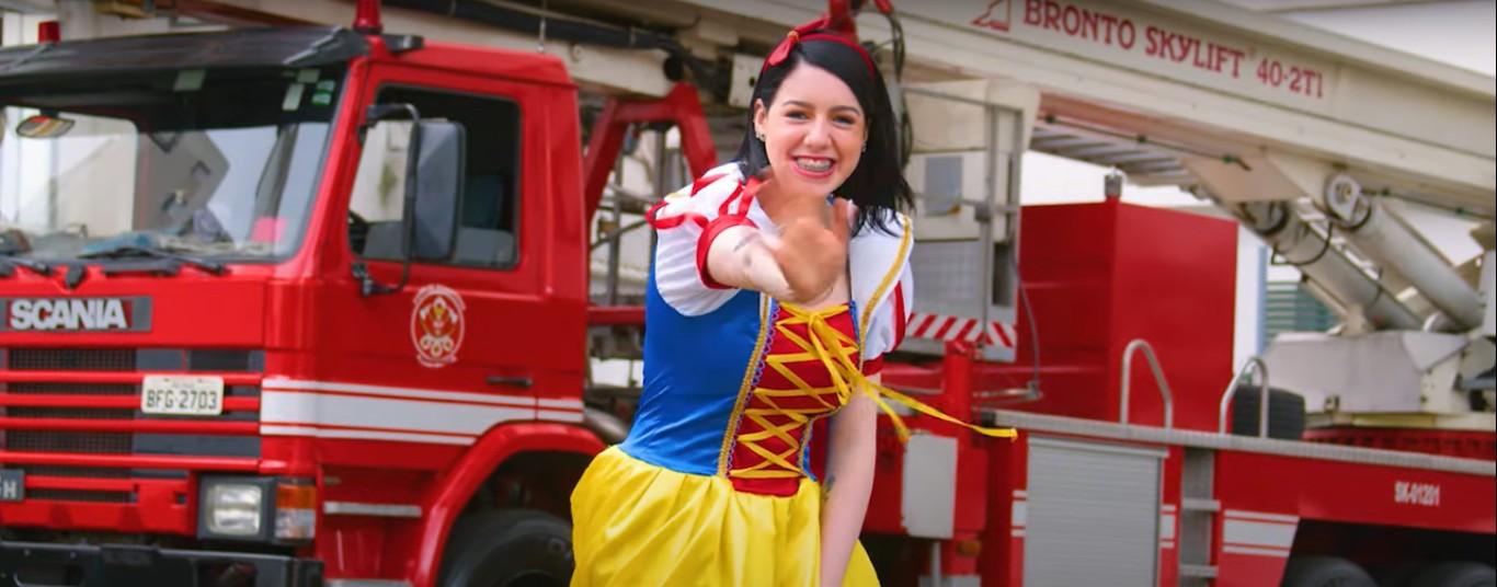 A imagem mostra a bombeira civil do A.C.Camargo fantasiada como a personagem Branca de Neve, com o caminhão dos bombeiros ao fundo