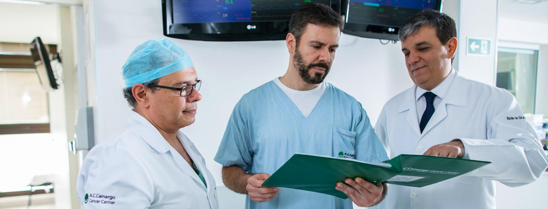 Três médicos analisando uma prancheta em uma sala cirúrgica