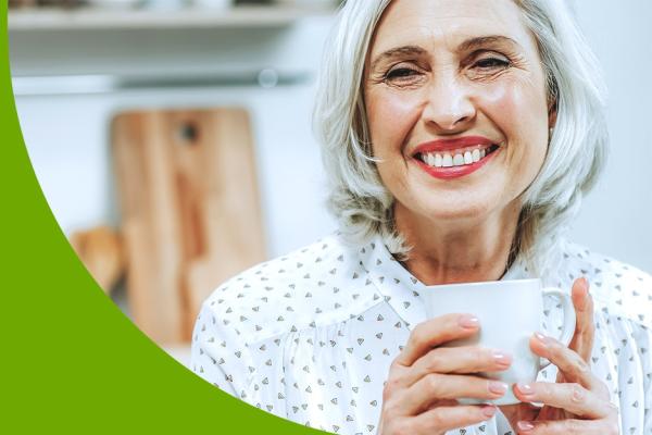 Mulher de cabelo branco sorri com seu batom vermelho e uma caneca na mão 