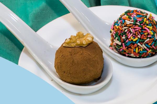 Duas colheres com duas bolinhas de brigadeiro, uma empanada no cacau em pó e outra com chocolate granulado colorido
