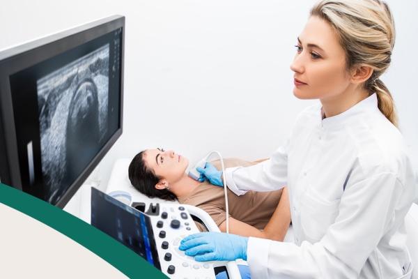 Médica fazendo ultrassom de tireoide em uma paciente mulher. Ambas são brancas e jovens.