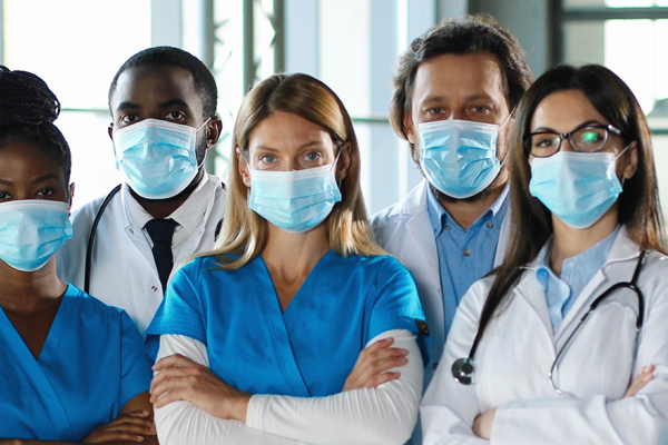 Uma equipe de profissionais de saúde de diferentes nacionalidades, todos com máscara e avental de médico