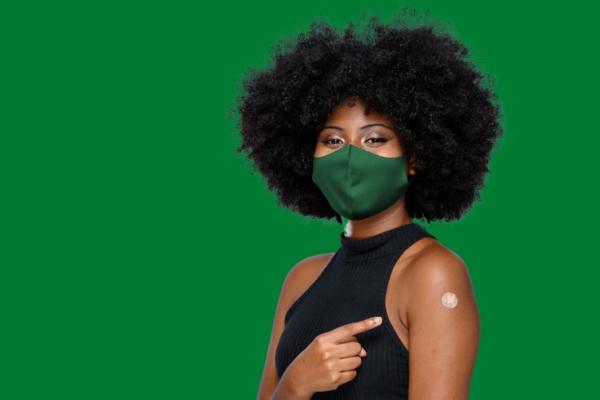 Mulher negra com máscara verde e braço vacinado, cabelo black power