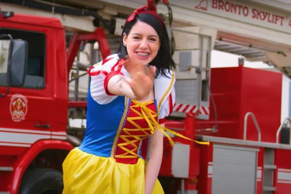 A imagem mostra a bombeira civil do A.C.Camargo fantasiada como a personagem Branca de Neve, com o caminhão dos bombeiros ao fundo