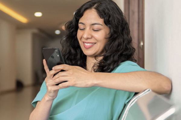Mulher com uniforme hospitalar olhando o celular e sorrindo