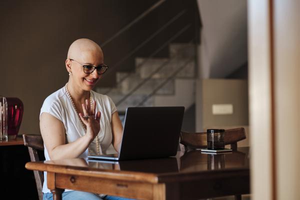 Mulher sentada à mesa dando tchau para alguém que está em vídeo no notebook