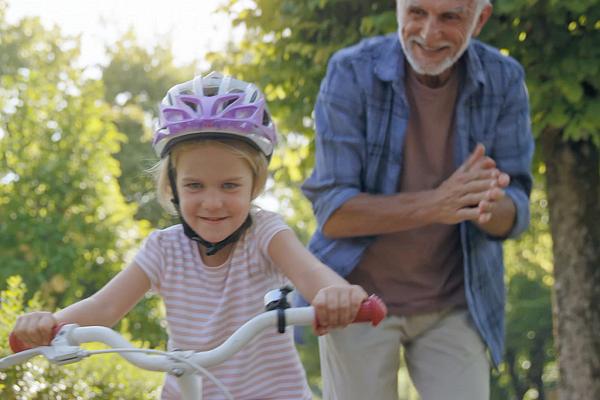 Imagem de um homem idoso aplaudindo e de uma menina aprendendo a andar de bicicleta