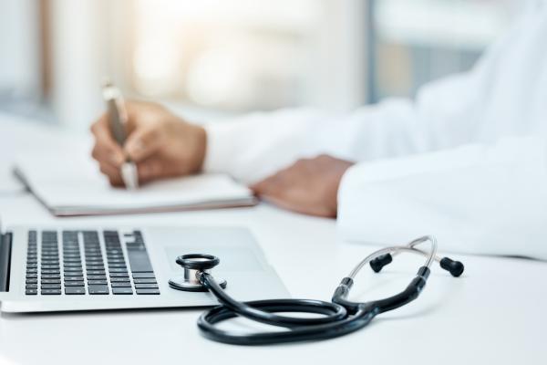 Médico fazendo uma pesquisa no notebook e anotando no caderno