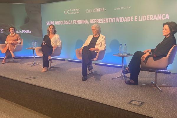Quatro mulheres se abraçando com roupas predominantemente rosa em um fundo verde