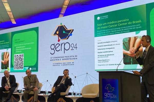 Quatro homens no palco de um evento palestrando sobre oncogeriatria