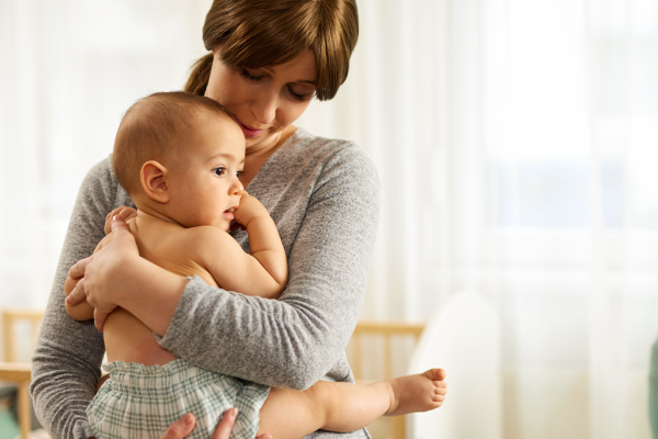 Bebê acordado e tranquilo no colo da mãe, junto a uma janela com luz natural.