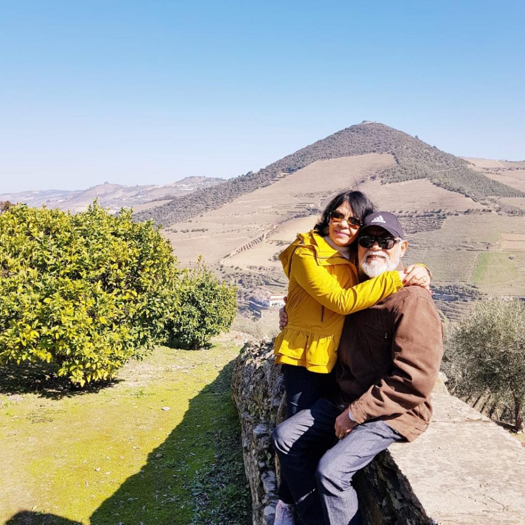Foto de Carlos e sua esposa sentados em um muro em uma paisagem montanhosa