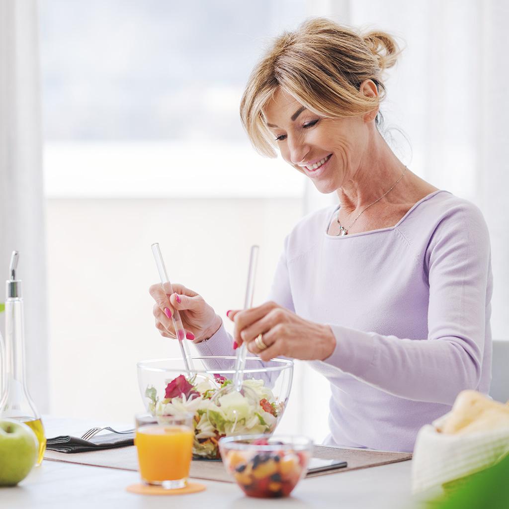 Uma mulher preparando uma salada em um recipiente de vidro