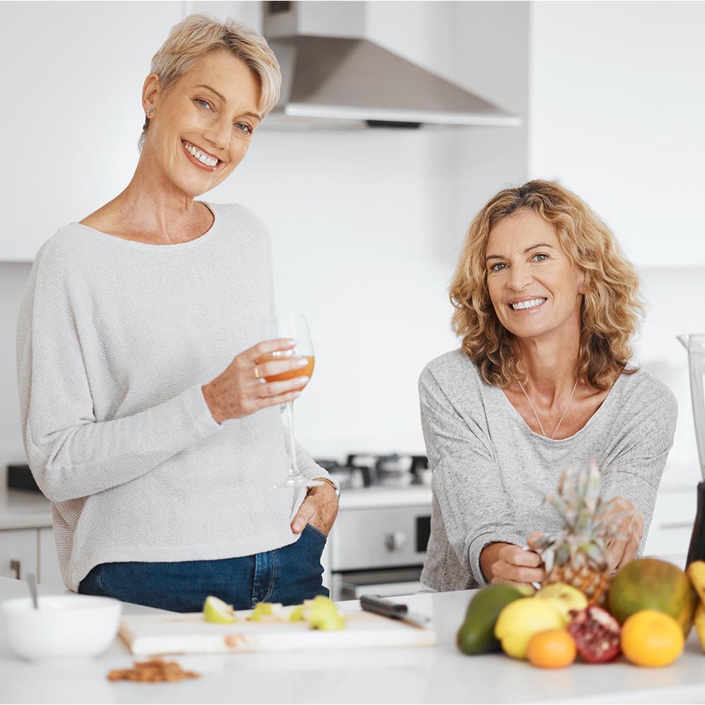 Duas mulheres em uma cozinha. Uma delas segura um copo
