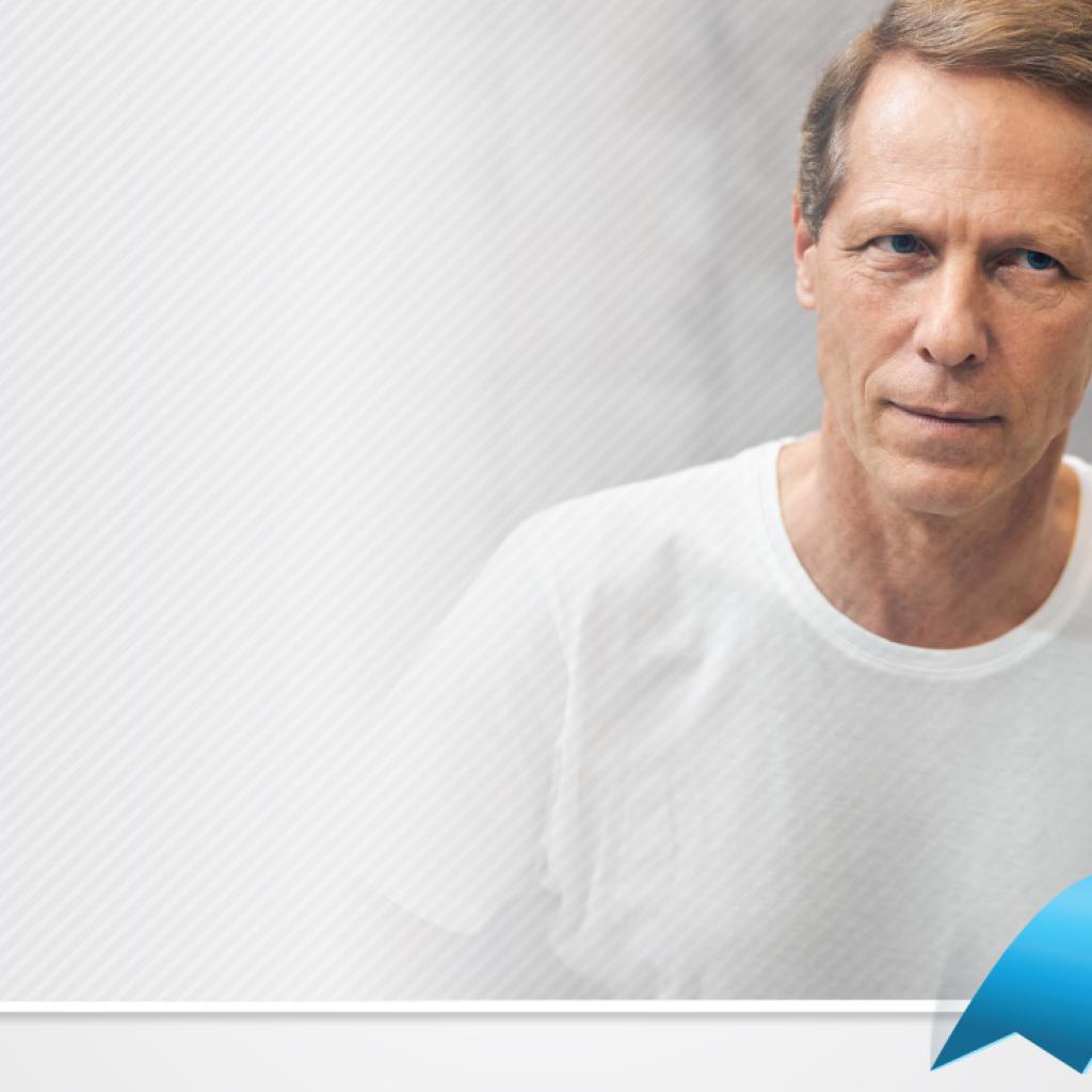 Homem branco de olhos azuis usando camiseta branca se olhando no espelho, no canto inferior direito, um laço azul colocado digitalmente na imagem