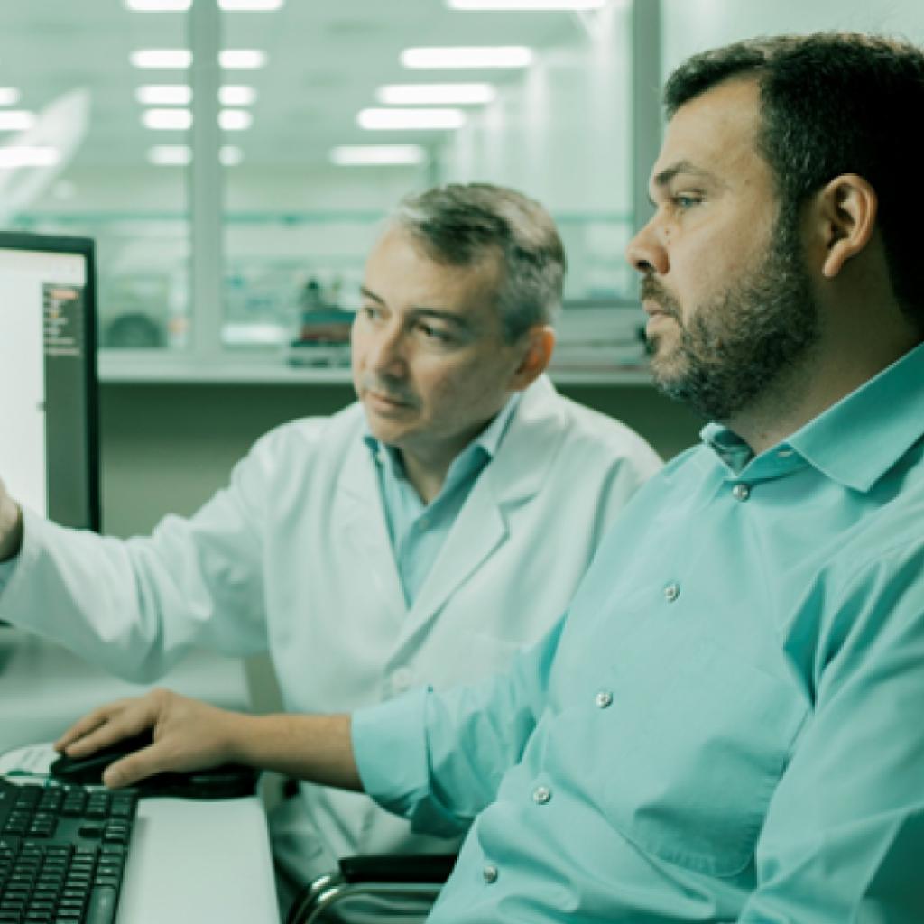 Doutor Israel e Doutor Helano, brancos, conversam diante do computador