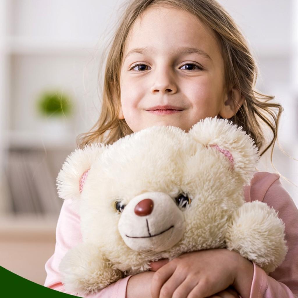 Arte gráfica em fundo verde escuro com uma foto cortada de uma criança branca loira segurando um urso. Uma mulher está ao fundo desfocada.