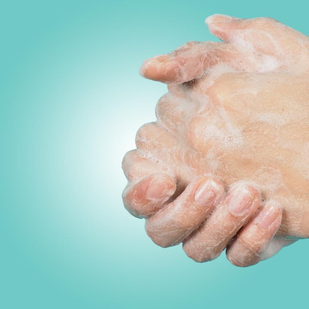 Duas mãos de uma pessoa branca ensaboadas e abraçadas em um fundo azul