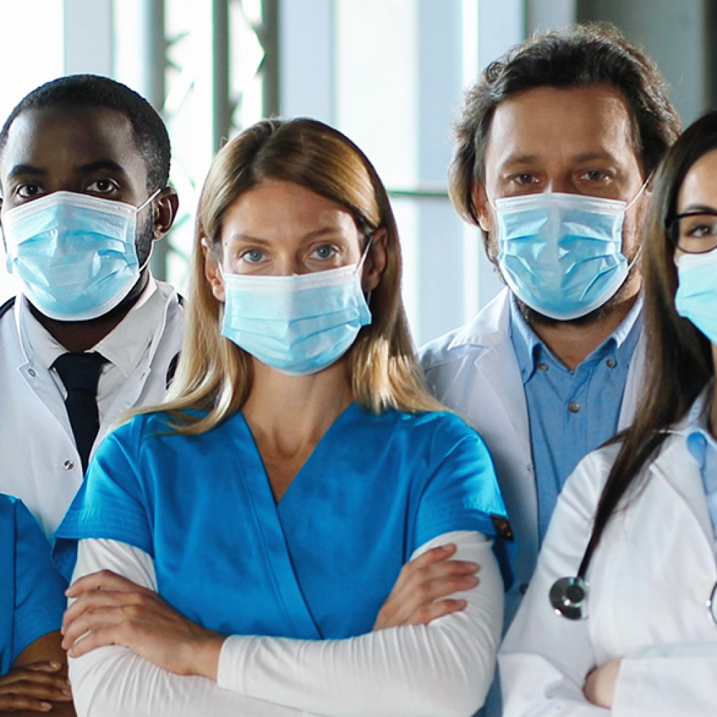 Uma equipe de profissionais de saúde de diferentes nacionalidades, todos com máscara e avental de médico