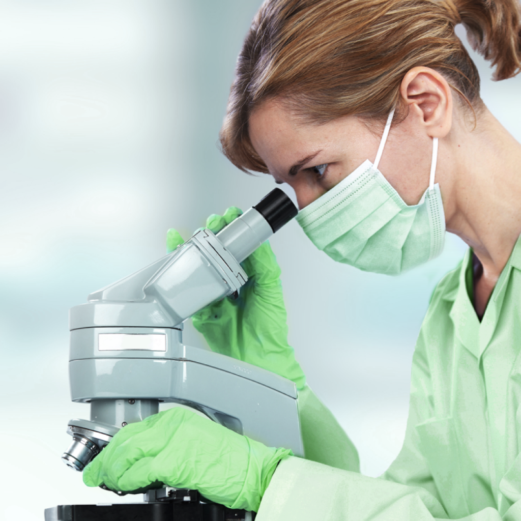 Cientista branca, cabelo castanho liso e avental mexendo em microscópio