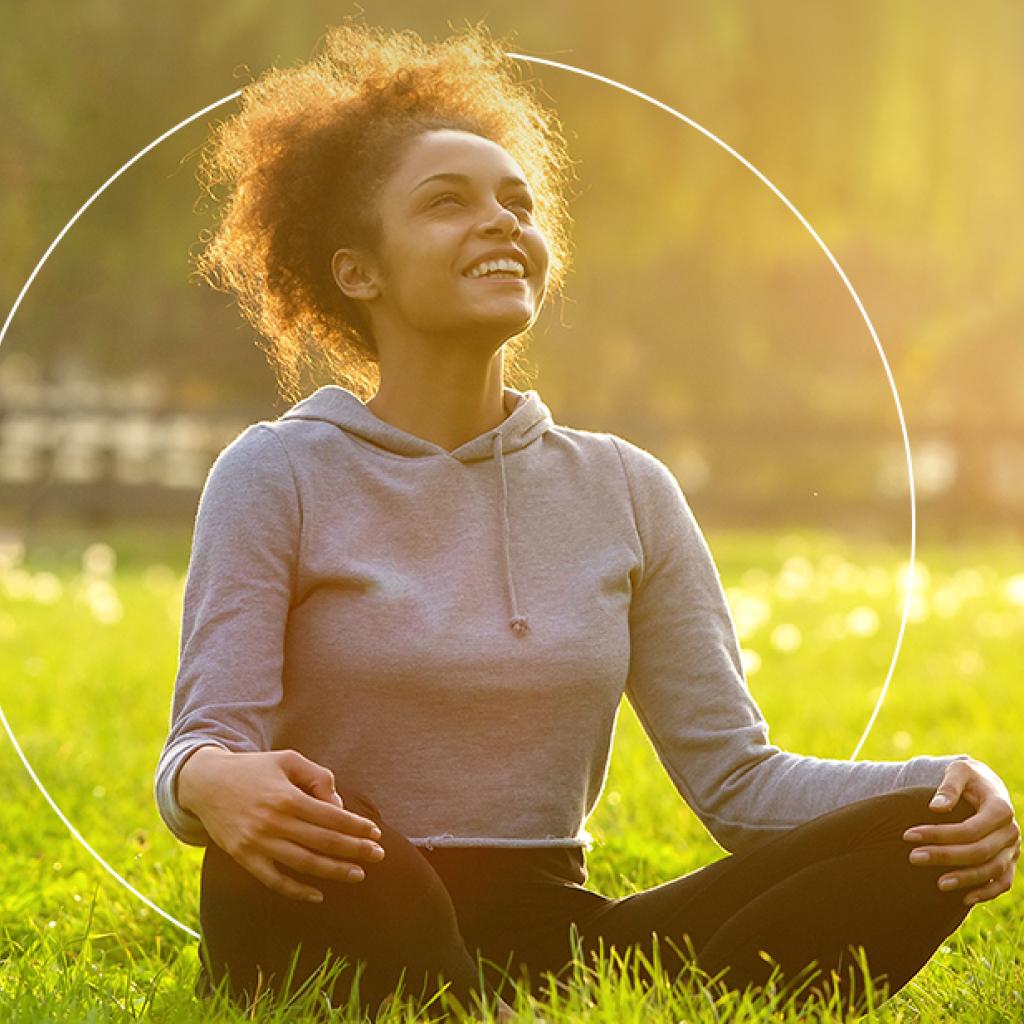 Jovem negra sorri meditando num parque