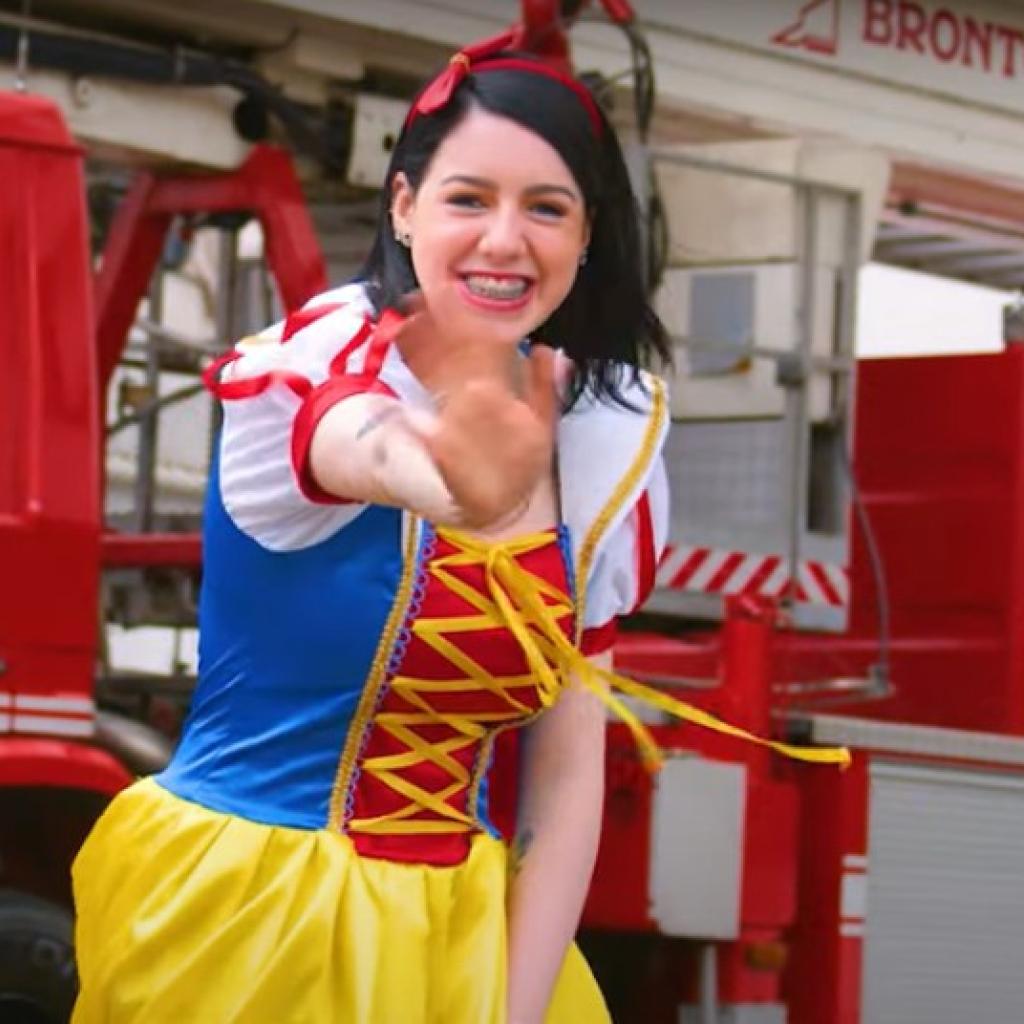 A imagem mostra a bombeira civil do A.C.Camargo fantasiada como a personagem Branca de Neve, com o caminhão dos bombeiros ao fundo