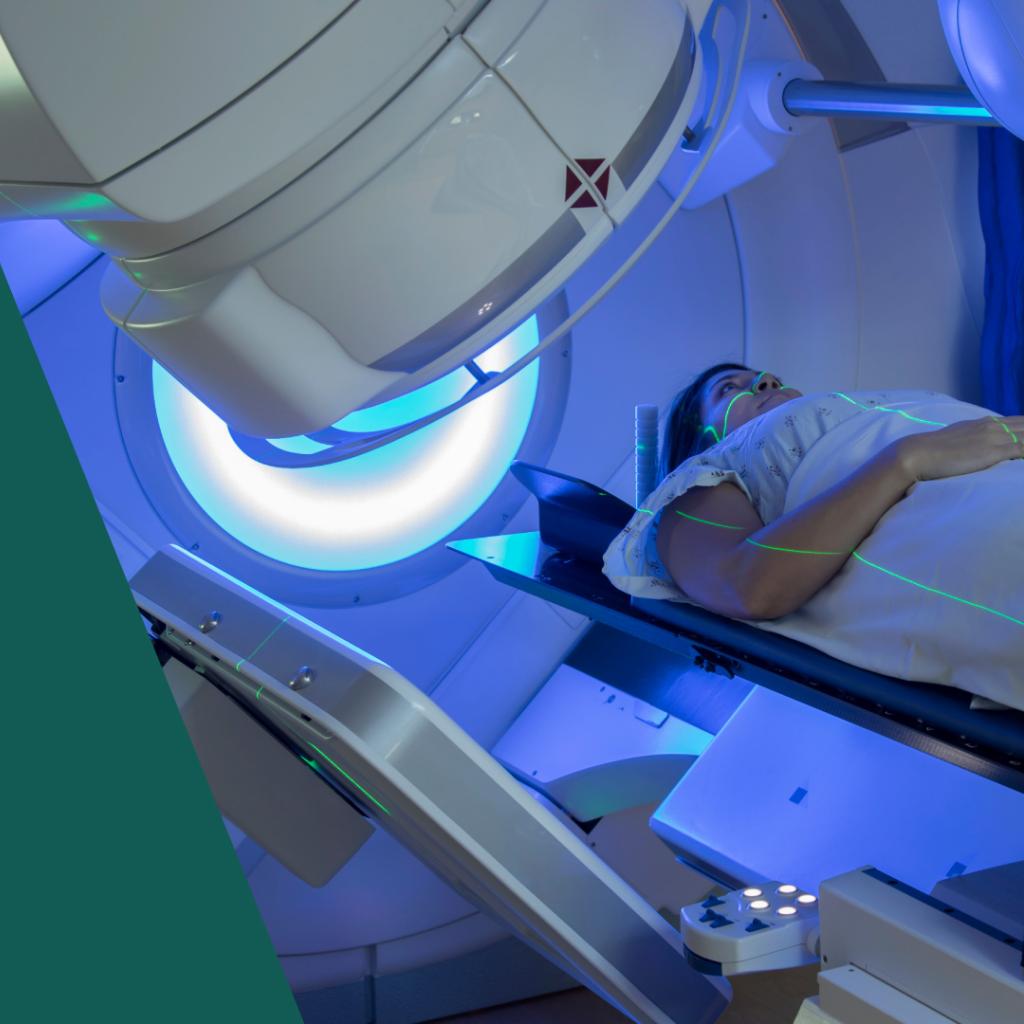 Mulher jovem branca deitada numa máquina branca de radioterapia, há objeto redondo com luz azul iluminando sua cabeça