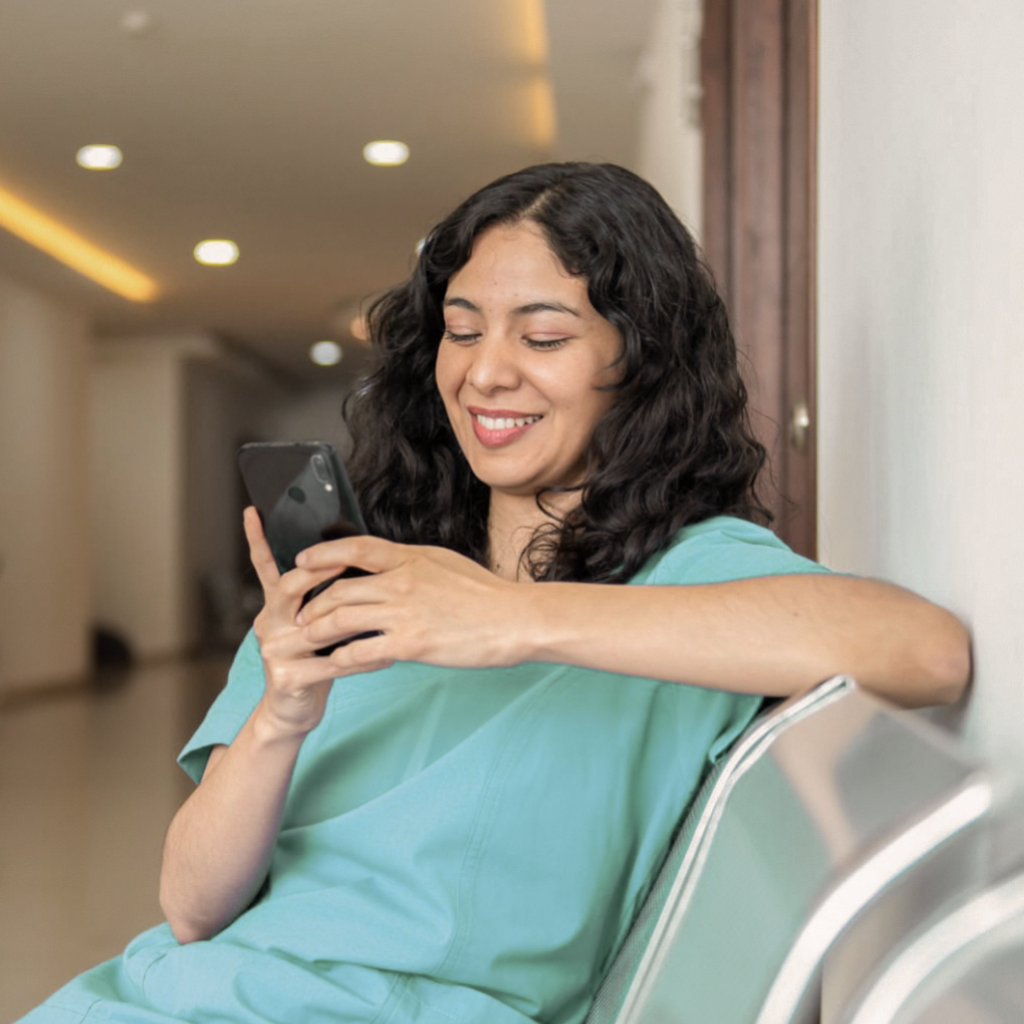 Mulher com uniforme hospitalar olhando o celular e sorrindo