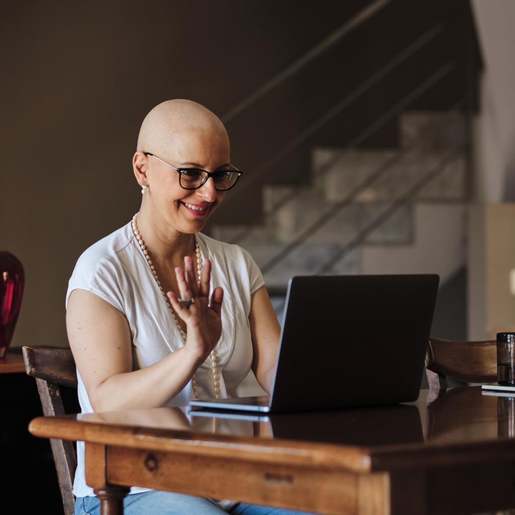 Mulher sentada à mesa dando tchau para alguém que está em vídeo no notebook