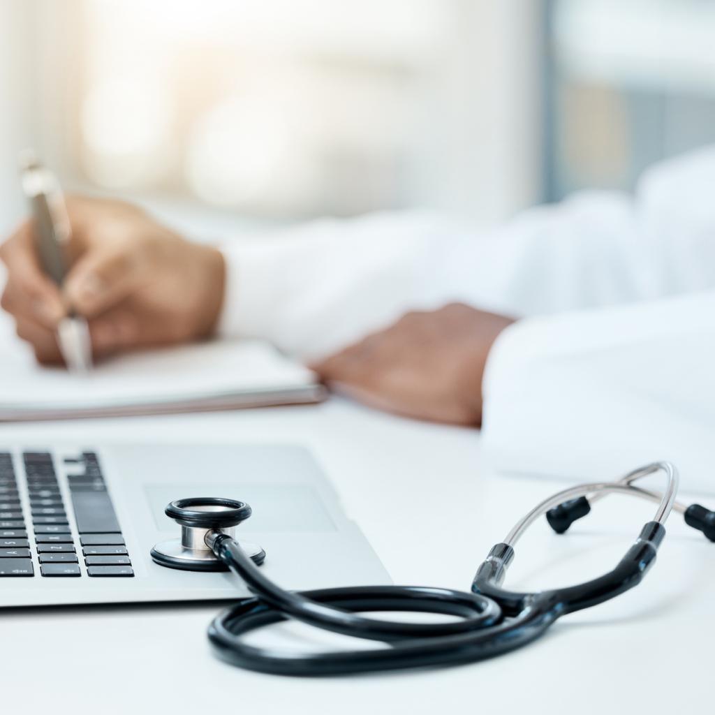 Médico fazendo uma pesquisa no notebook e anotando no caderno