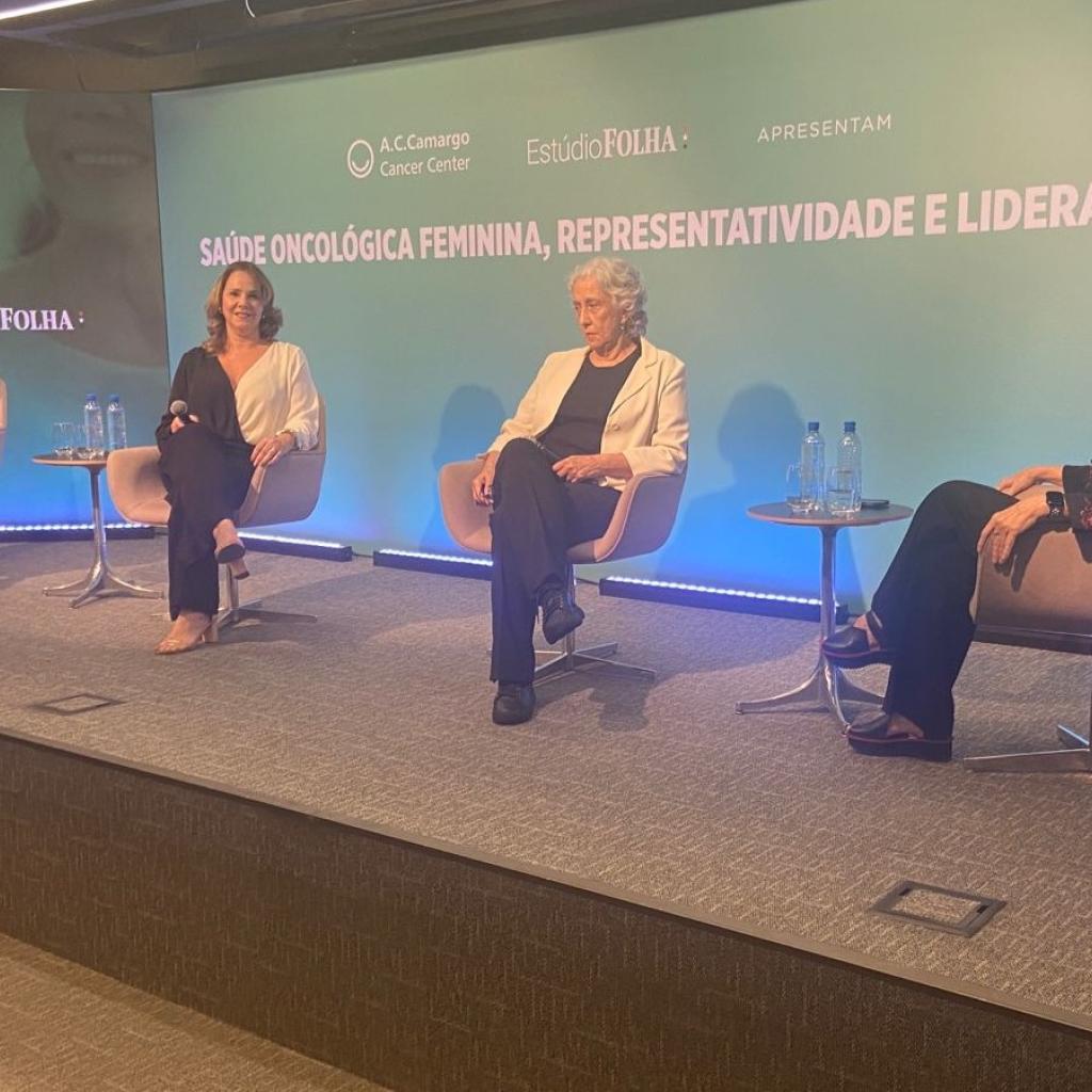 Quatro mulheres se abraçando com roupas predominantemente rosa em um fundo verde